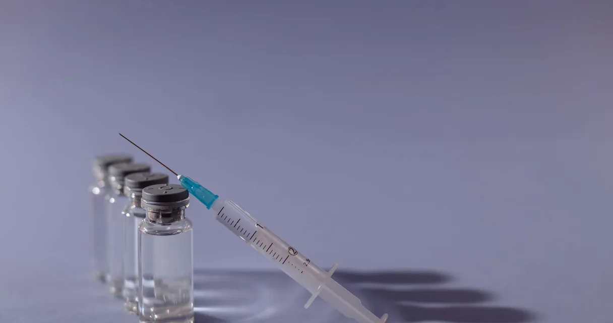 Frascos de vacina e uma seringa descartável sobre uma superfície azul clara